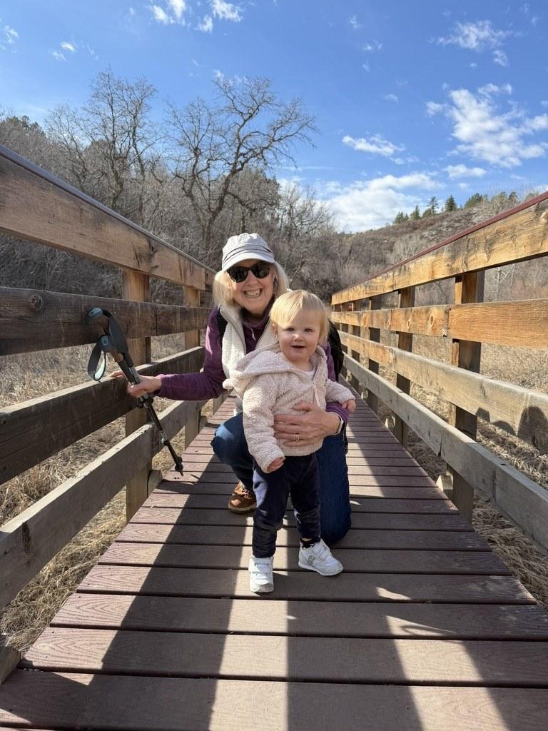 Nancy Elder on a wooden footbridge on a bright winter day, crouching beside a small child.